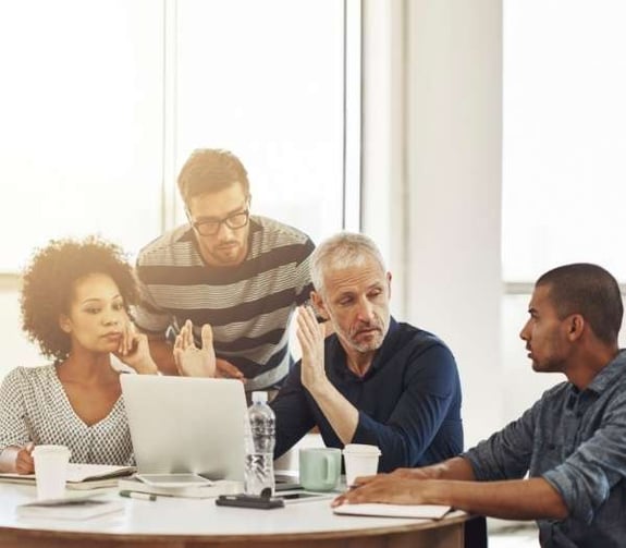 four professionals talking at a table with a laptop