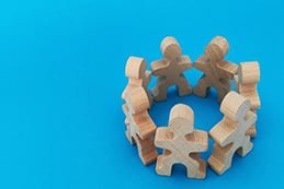 Teamwork and cooperation concept, wooden puzzle pieces that represent people stand in a circle on a blue background.